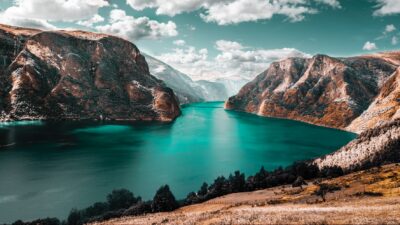 Turquoise fjord flanked by steep mountains with sparse vegetation under a partly cloudy sky.