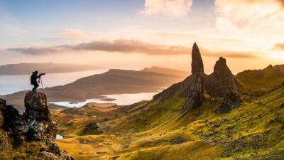 Landscape of green rolling hills and rocky formations at sunrise with water bodies in the distance.